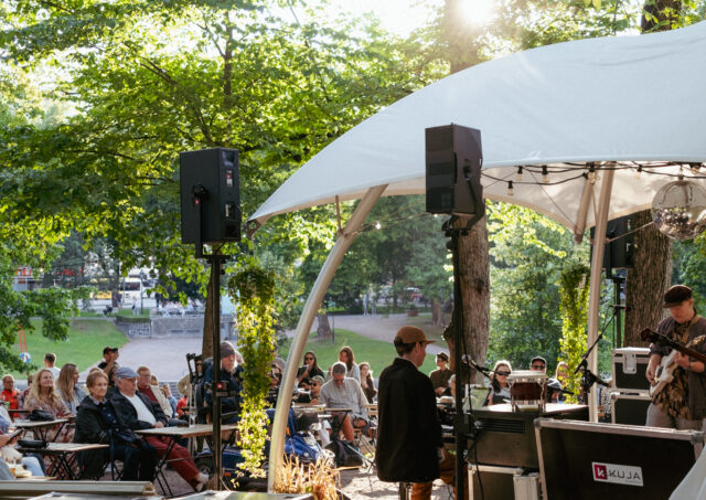 Kesäinen kuva Kirkkopuiston Terassilta, jossa lavalla muusikoita ja taustalla yleisöä