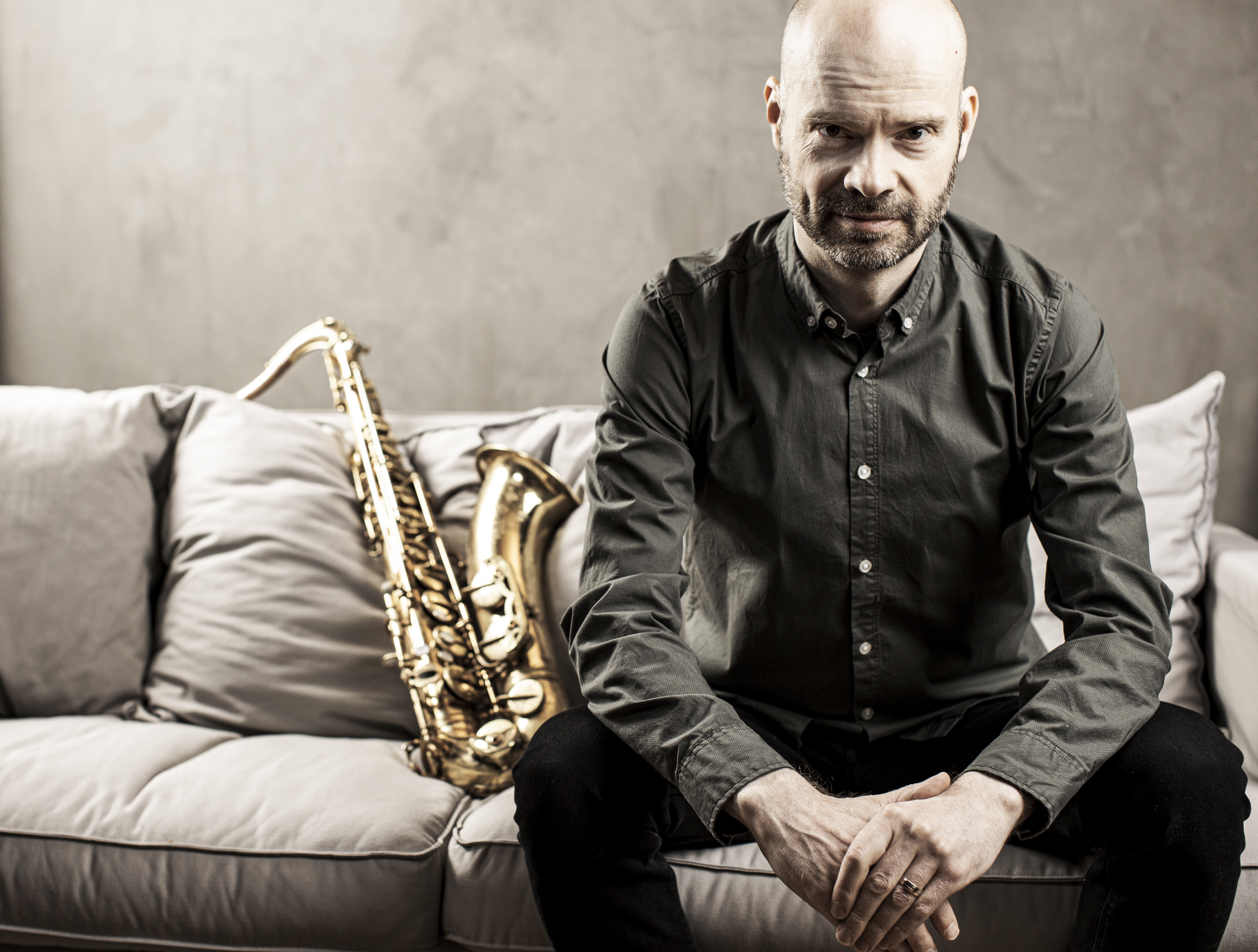 Mies istuu sohvalla vieressään saksofoni.