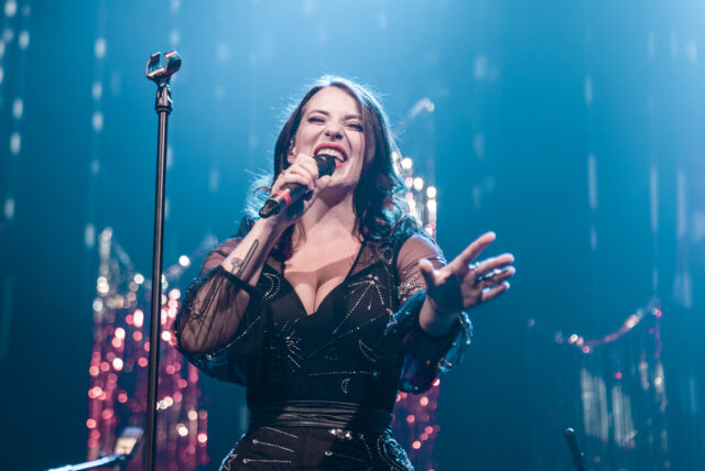 Hymyilevä nainen laulaa mikrofoniin esiintymislavalla.